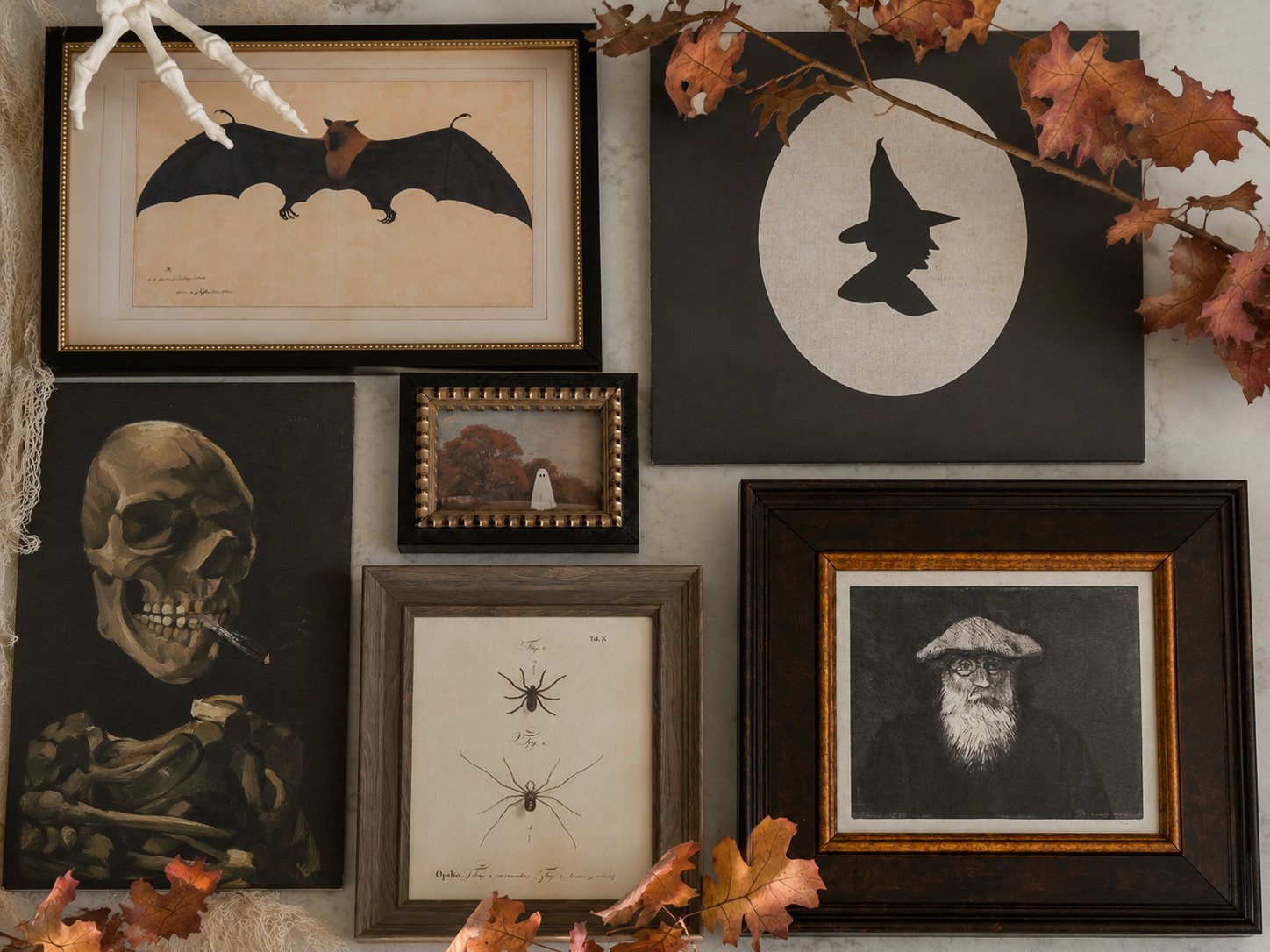 A collection of five framed gothic and Halloween wall art prints arranged on a textured wall with autumn leaves and a white bone decoration.